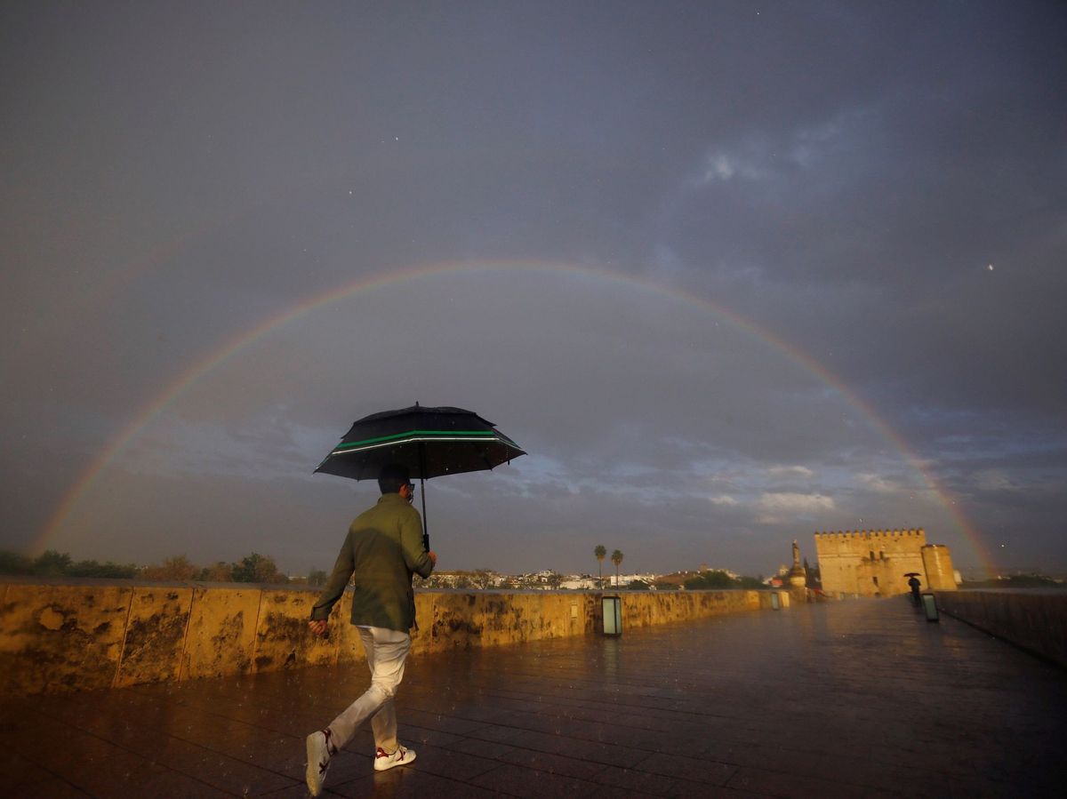 Foto: Un transeúnte se protege con un paraguas en el Puente Romano de Córdoba (EFE)