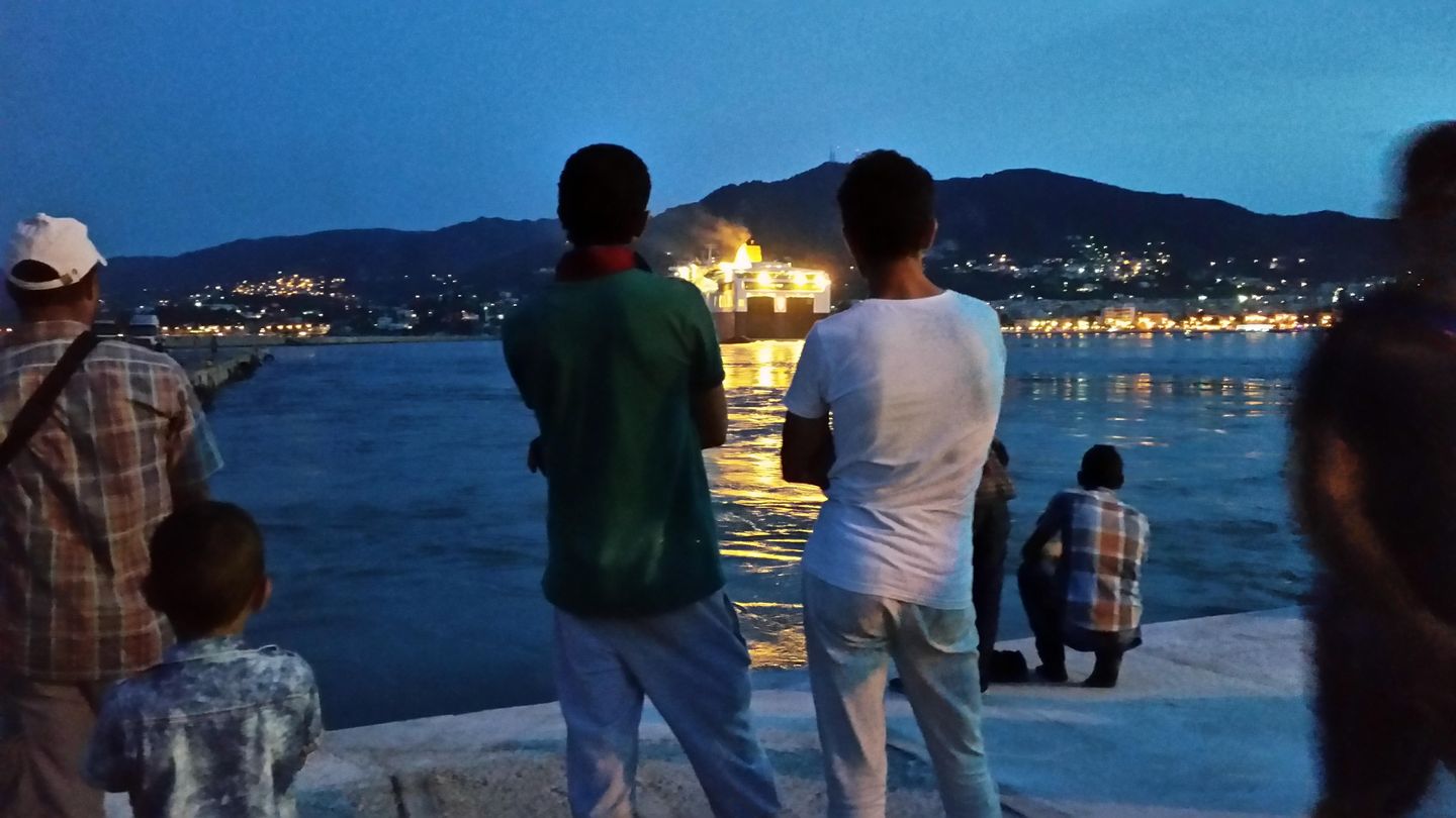 Dos refugiados sirios observan los ferris que parten hacia el Pireo desde la isla de Lesbos. (Foto: P. Cebrián)