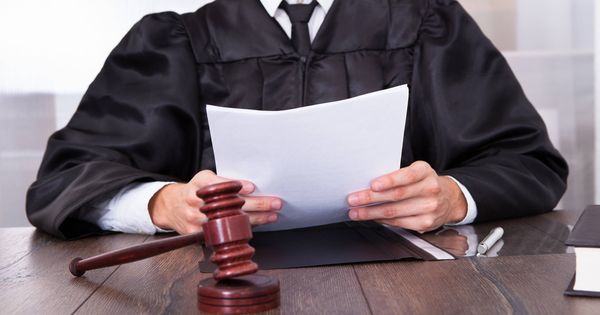 Foto: Un juez sostiene varios documentos con un mazo sobre la mesa.