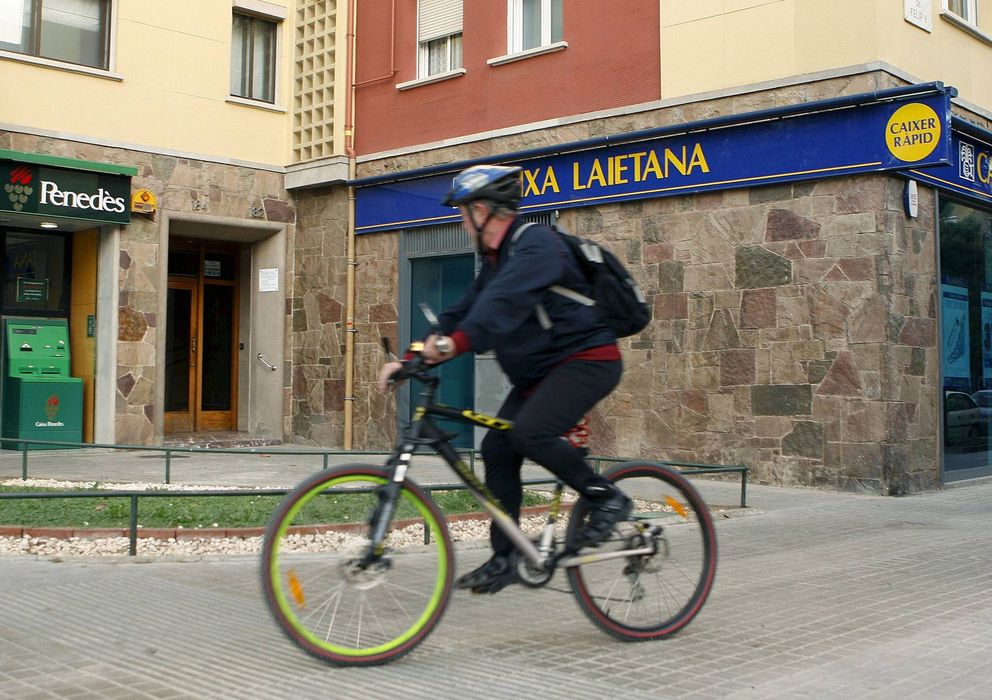 Foto: Un hombre pasa en bicicleta ante sucursales de Caixa Penedès y Caixa Laietana. (EFE)