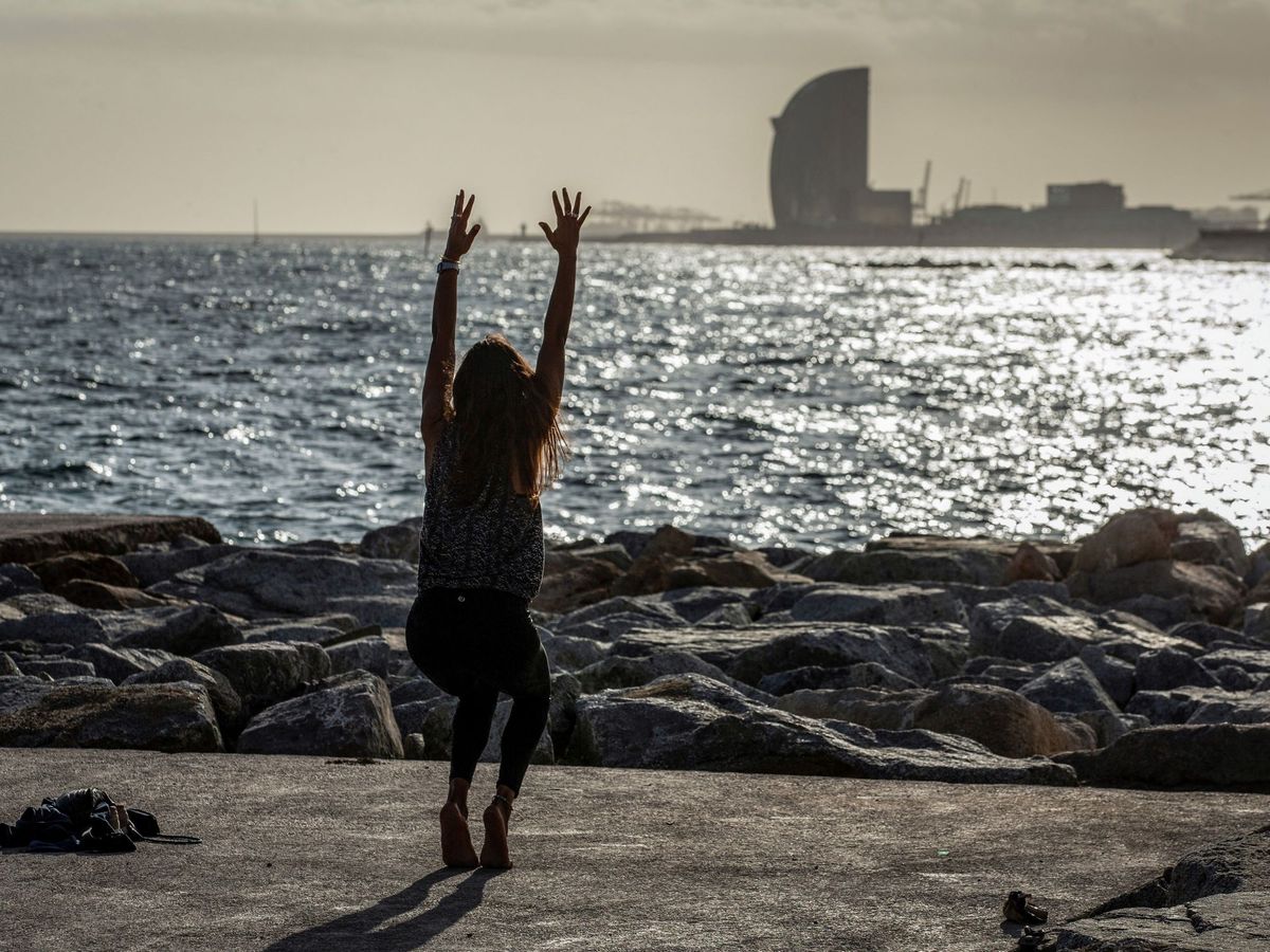 Foto: Una mujer hace ejercicios de yoga cerca de la playa de Mar Bella en Barcelona. (EFE)