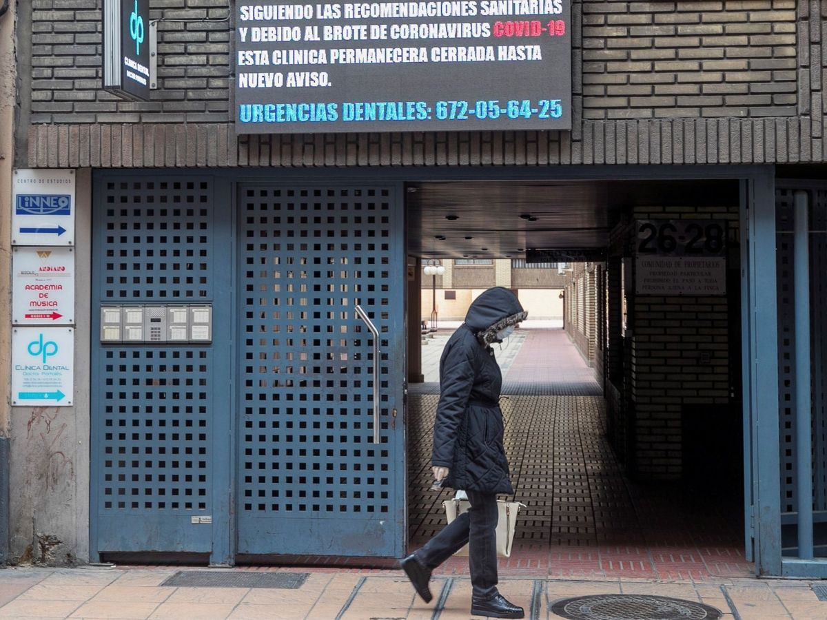 Foto: Una mujer camina ante una clínica dental que informa a sus pacientes del cierre de la misma en Zaragoza (EFE)