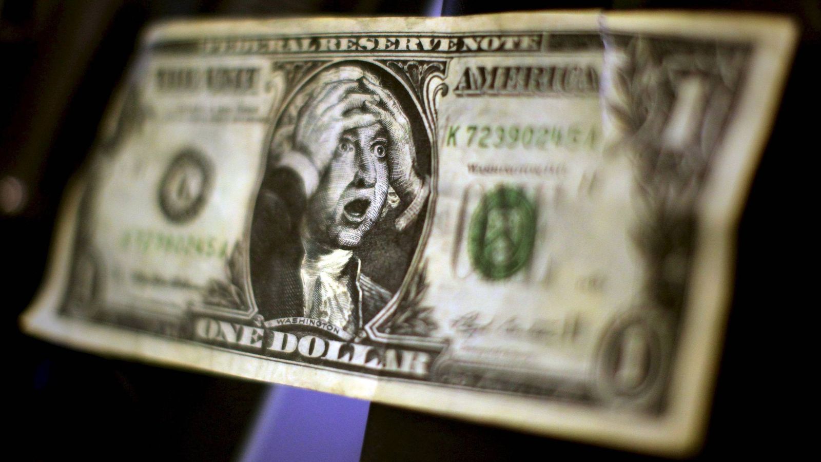 Foto: Un billete de un dolar falso con la imagen de George Washington llevandose las manos a la cabeza. (EFE)