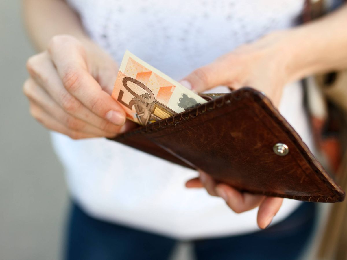 Foto: Una mujer saca dinero de la cartera. (iStock)