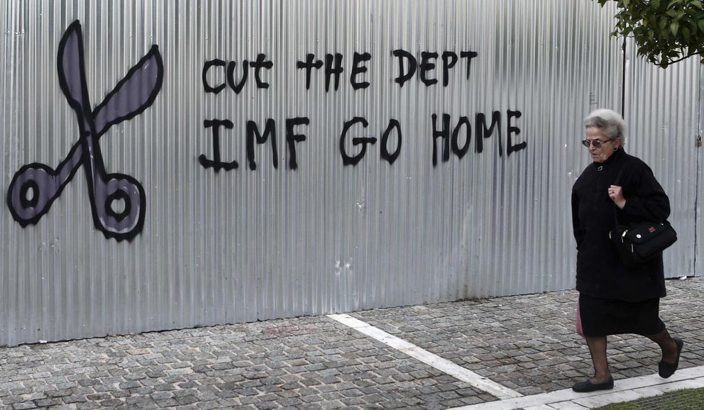 Una mujer pasea frente a una pintada en Atenas contra el FMI (Reuters)