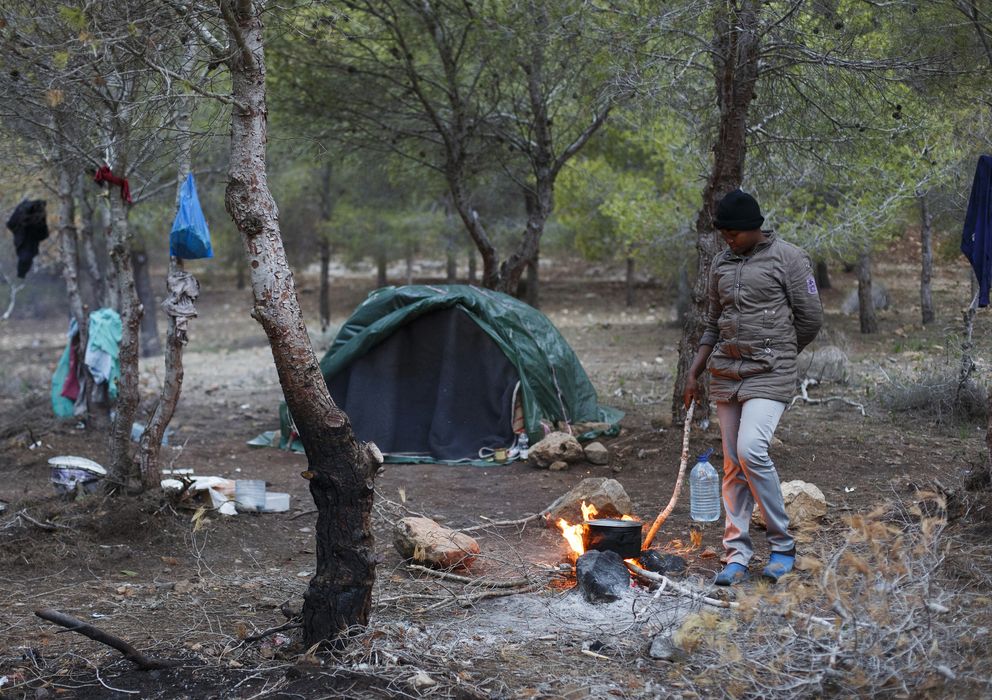 Foto: Marie, de Camerún, aviva un fuego en el campamento clandestino de Bolingo, frente a Melilla (Reuters).