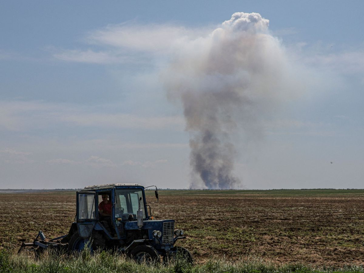 Foto: Un trabajador agrícola conduce un tractor mientras el humo se eleva en la distancia tras un ataque militar. (Reuters/Andrii Dubchak)
