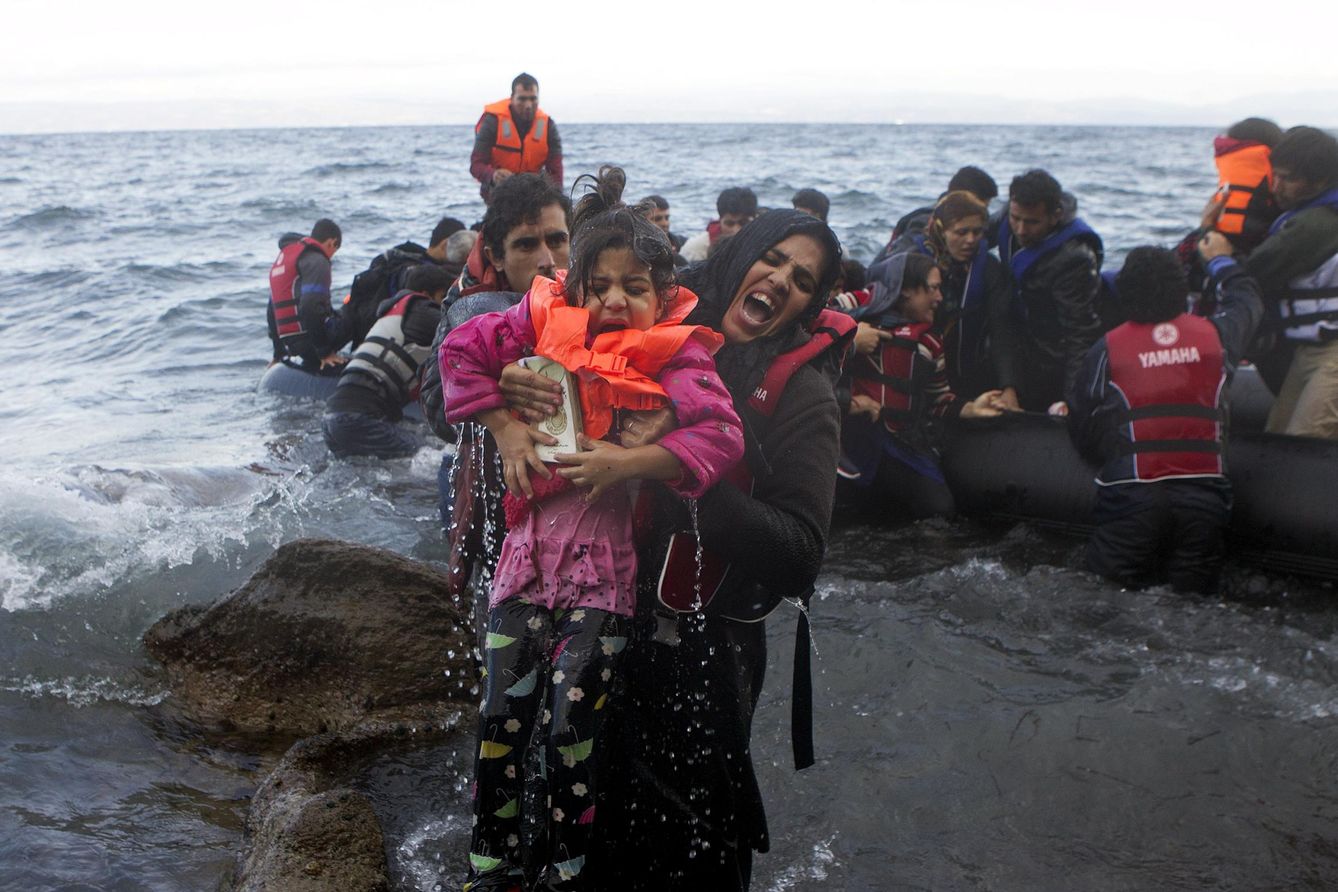 Una mujer saca a una niña del agua cuando refugiados e inmigrantes alcanzan la isla griega de Lesbos. (Reuters)