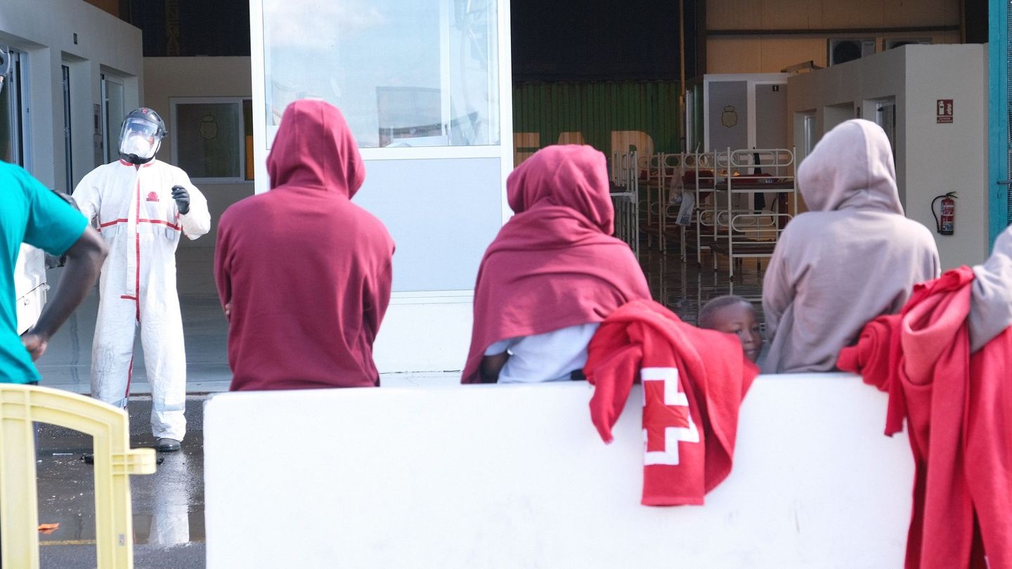 Los 39 inmigrantes que llegaron en patera a Fuerteventura esperan fuera de la nave del muelle de Puerto del Rosario donde pasan desde entonces la cuarentena a que se desinfecten esas instalaciones, después de que 14 de ellos dieran positivo en covid-19. (EFE)