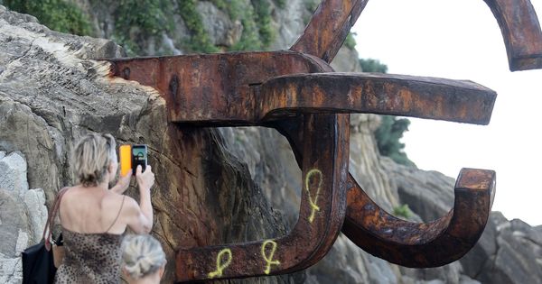 Foto: Una turista fotografía la obra de Chillida con los tres lazos amarillos pintados. (EFE)