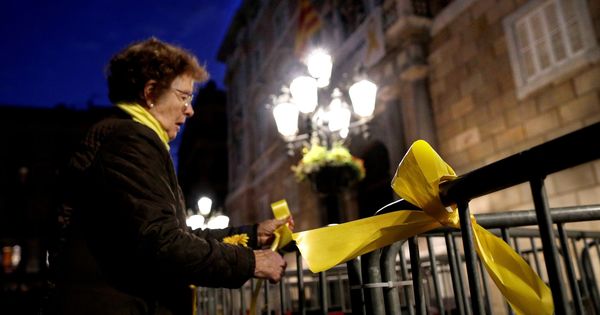 Foto: Una mujer coloca lazos amarillos en las vallas que rodean el Palau de la Generalitat en cuya fachada permanece la pancarta que pide la liberación de los políticos presos y un lazo amarillo. (EFE)