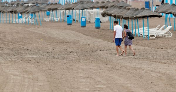 Foto: Una pareja pasea por la playa de la Malvarrosa en la que la afluencia de gente ha descendido notablemente debido en gran medida al descenso de temperaturas, a los chubascos y al cielo nublado. (EFE)