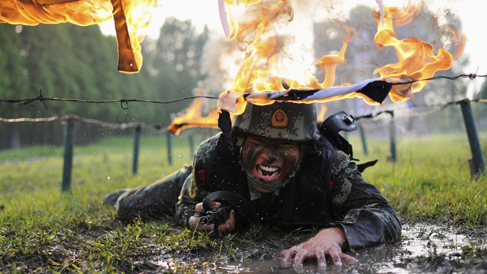 Foto: Un policía paramilitar se arrastra bajo obstáculos en llamas durante un entrenamiento en una base de Chanou, China. (Reuters)