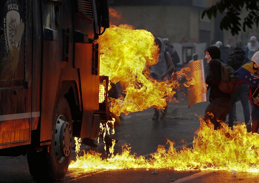 Foto: Manifestantes se protegen de las llamas cerca de un cañón de agua de la policía durante protestas en Caracas, Venezuela. (Reuters)