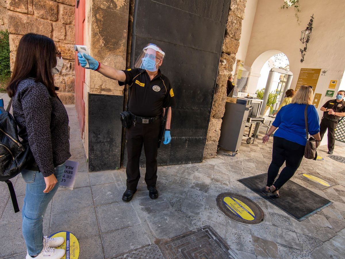 Foto: Un guardia de seguridad toma la temperatura a una joven en la Puerta del León del Real Alcázar de Sevilla. (EFE)