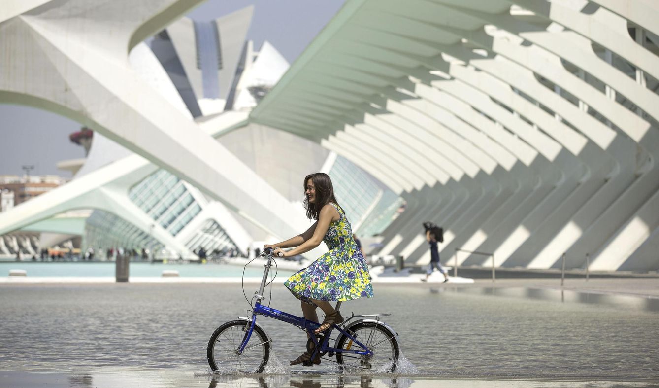 Una joven pasea con su bicicleta por una de las láminas de agua de la Ciudad de las Artes y las Ciencias. (EFE)