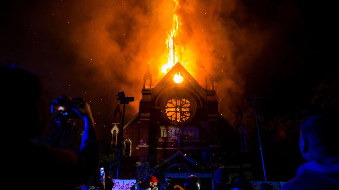 Un grupo de manifestantes observa como arde la iglesia de San Francisco de Borja, actualmente destinada al servicio religioso de Carabineros de Chile, este domingo durante una manifestación en los alrededores de la Plaza Italia de Santiago (Chile). EFE