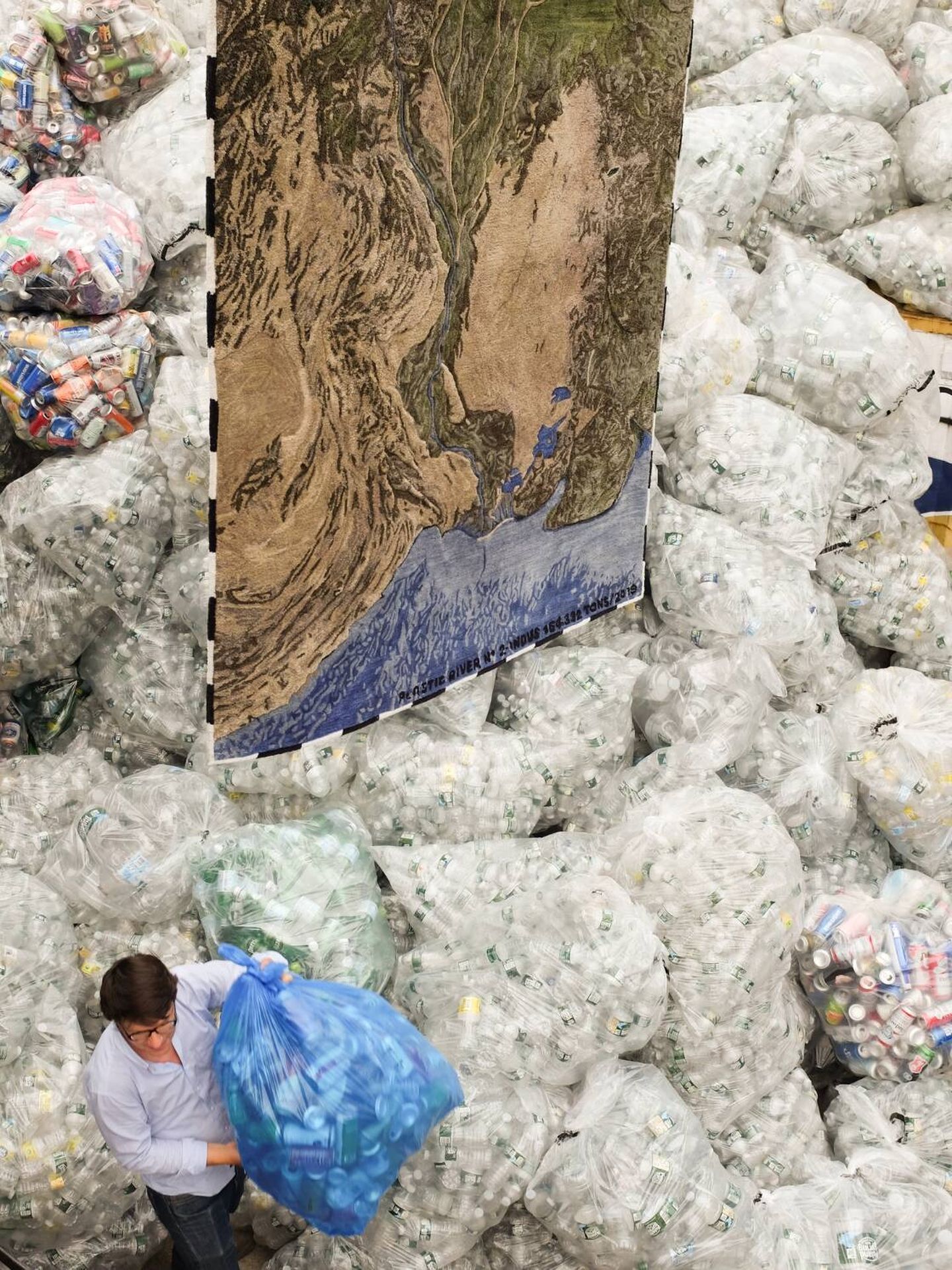 Álvaro Catalán de Ocón posa junto a una de sus alfombras Plastic Rivers rodeado de bolsas de desechos. (Cortesía)