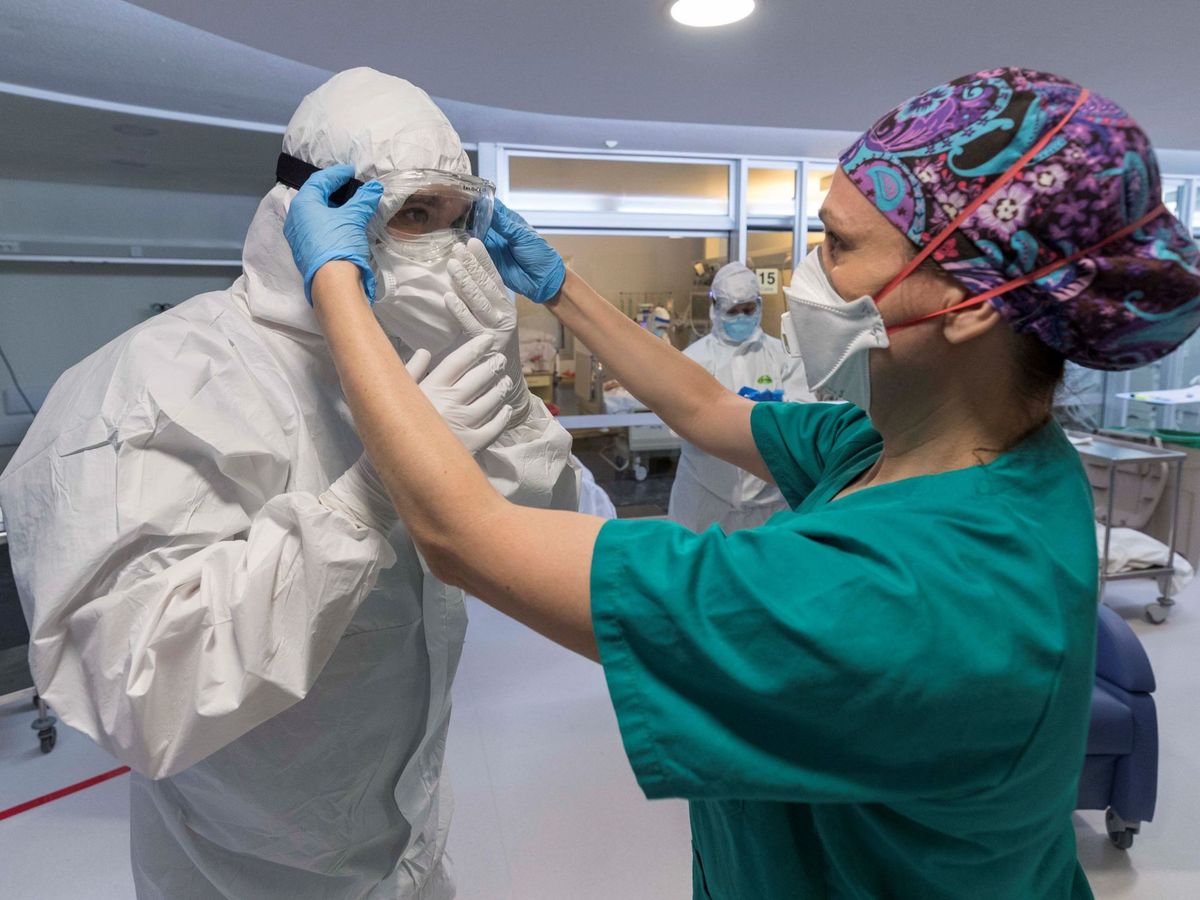 Foto: Una enfermera de la unidad de cuidados intensivos ayuda a un compañero a colocarse las protecciones. (EFE)