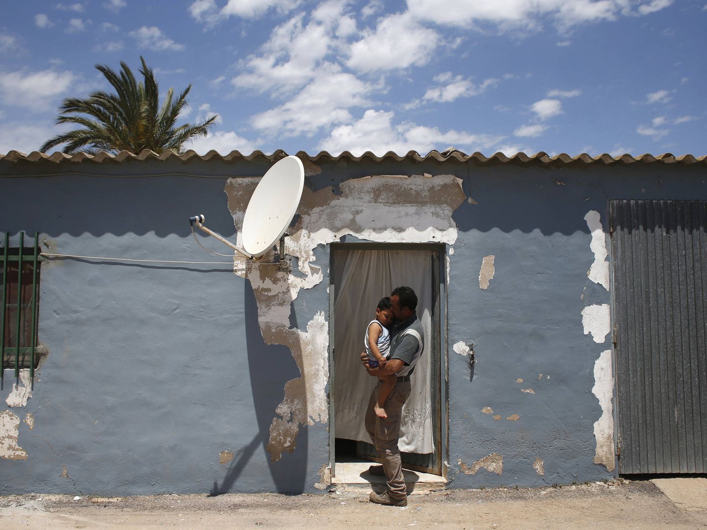 Un jornalero marroquí sostiene a su hijo en una vivienda dentro de una explotación en el campo de Cartagena. (Reuters)