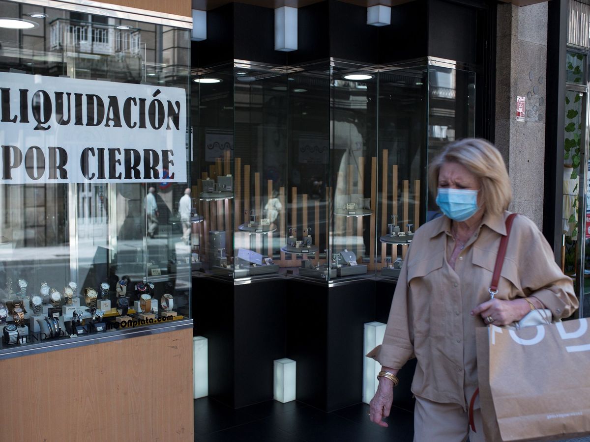 Foto: Una mujer con mascarilla pasa ante un comercio con un cartel de "liquidación por cierre" en Ourense. (EFE)