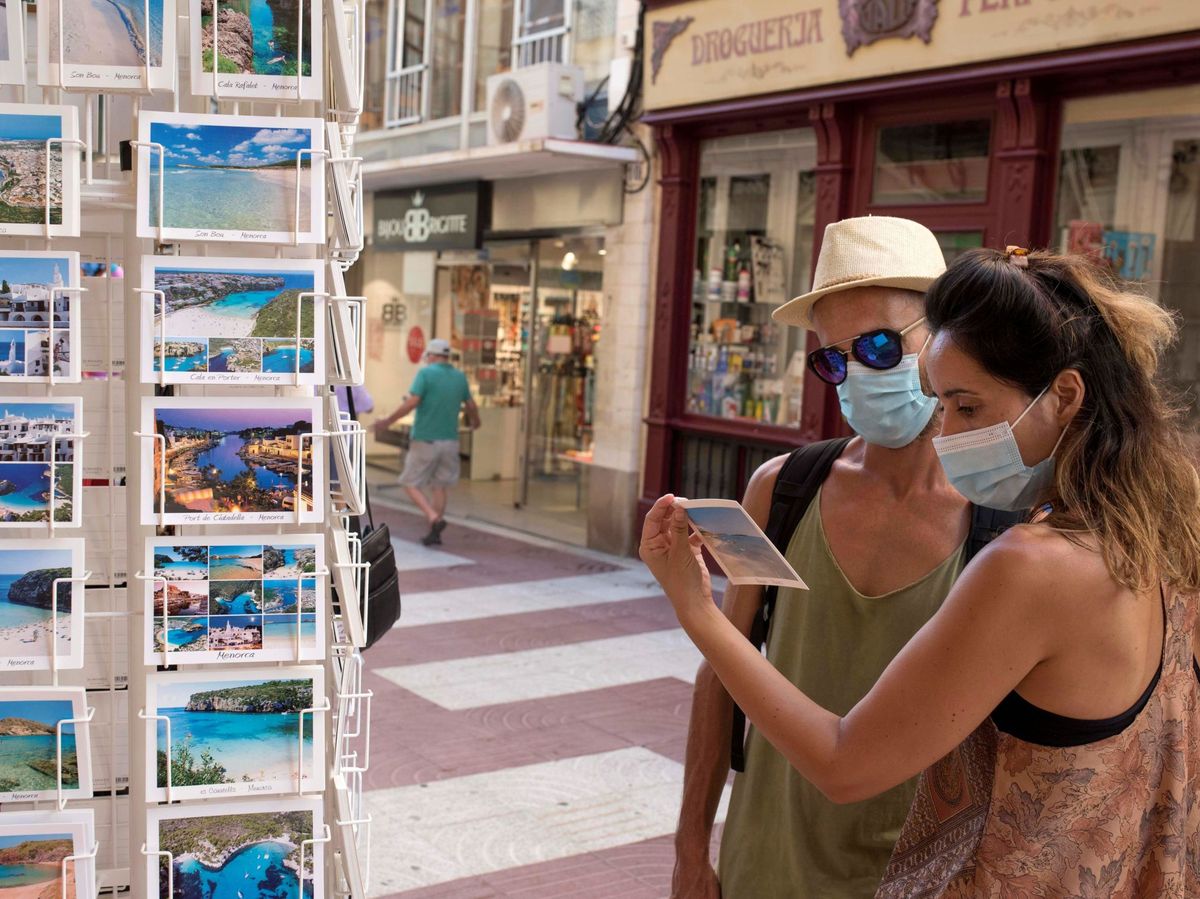 Foto: Varios turistas ojean postales en un puesto de Menorca. (EFE)