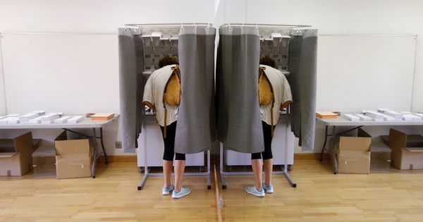 Foto: Un elector, con su imagen reflejada en un espejo, elige su papeleta para ejercer su derecho al voto. (EFE)