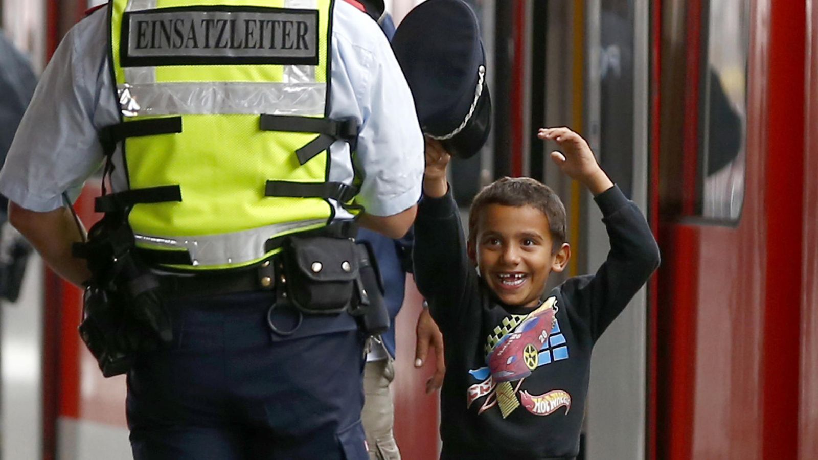 Foto: Un niño refugiado juega con la gorra de un policía austriaco (Reuters).