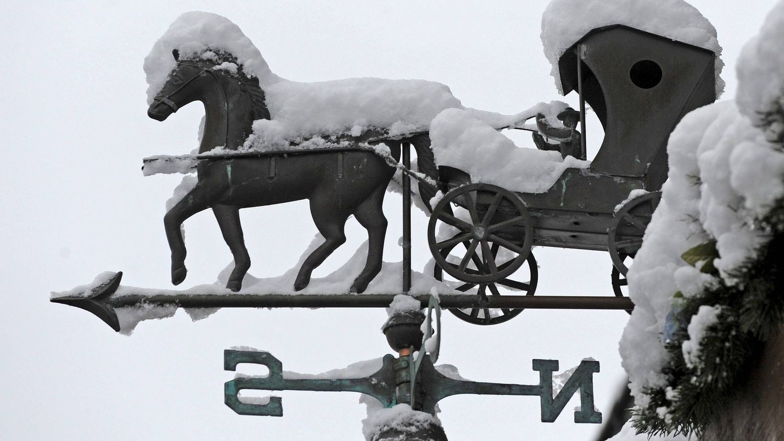 Foto: La nieve cubre parte de una veleta con forma de coche de caballos en el tejado de una vivienda. (EFE)
