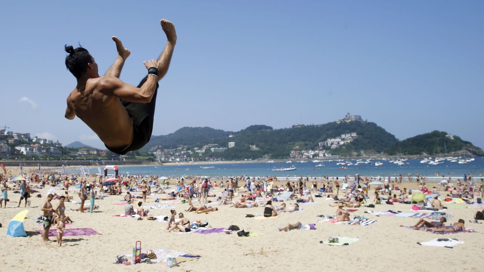 Foto: Un joven realiza un salto acrobático en la playa de La Concha. (EFE)
