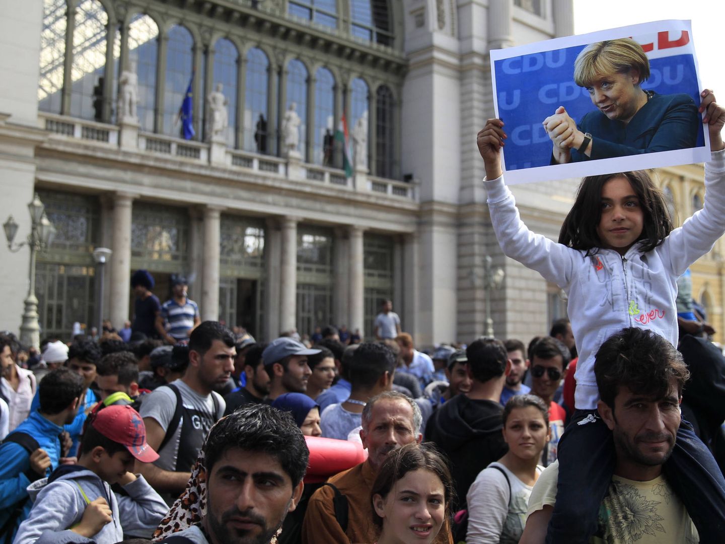Un niña muestra una imagen de Merkel mientras un grupo de migrantes se dirige a la frontera austriaca, en Budapest, en septiembre de 2015. (Reuters) 