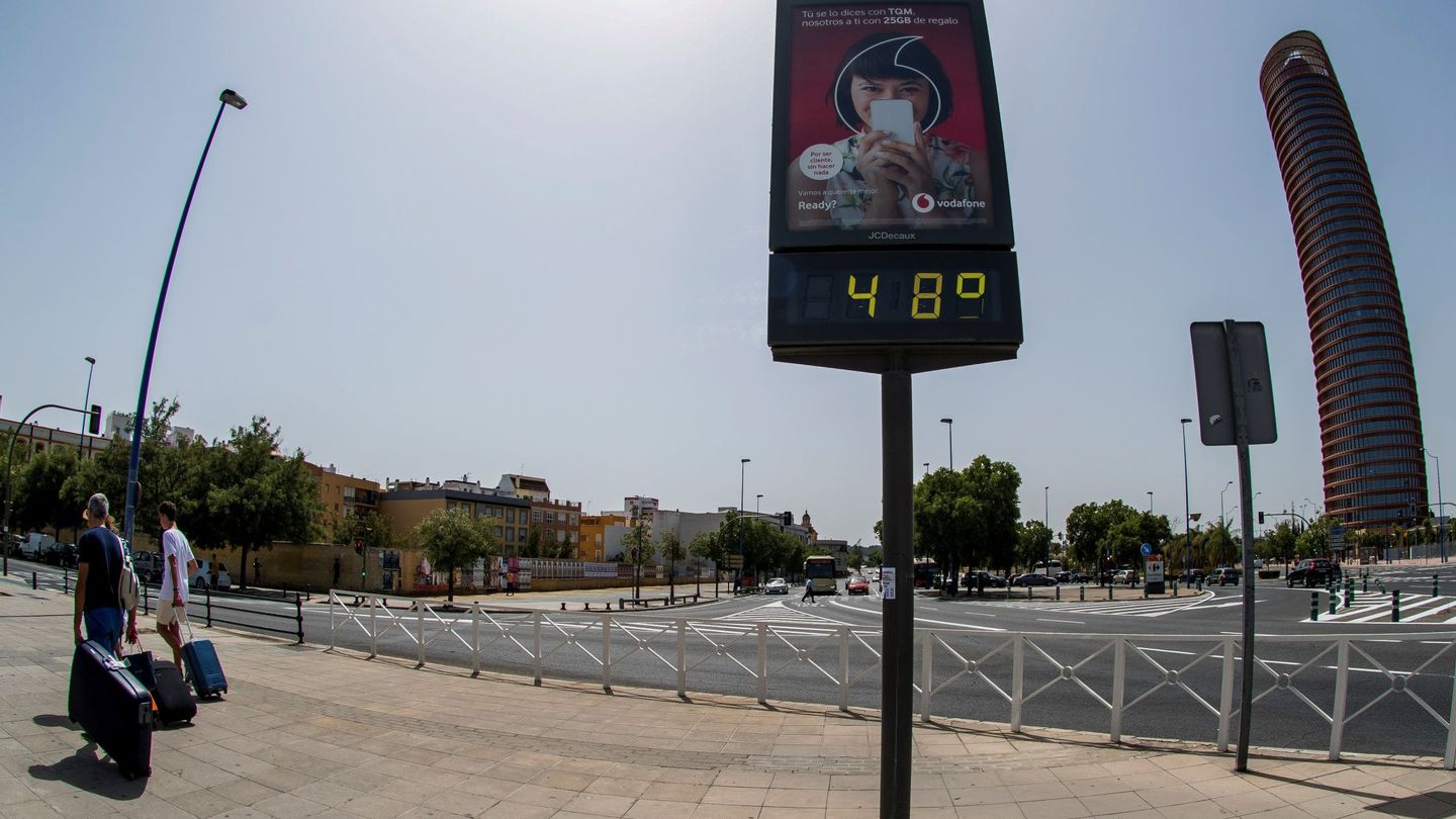 Turistas pasan junto a un termómetro de Sevilla que marca 48ºC. (EFE)