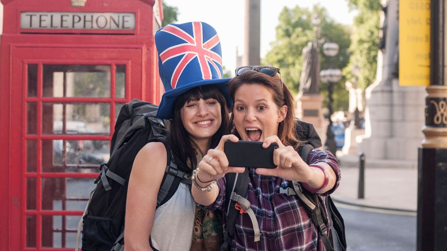 Two women backpackers taking smartphone selfie at red telephone box, London, UK