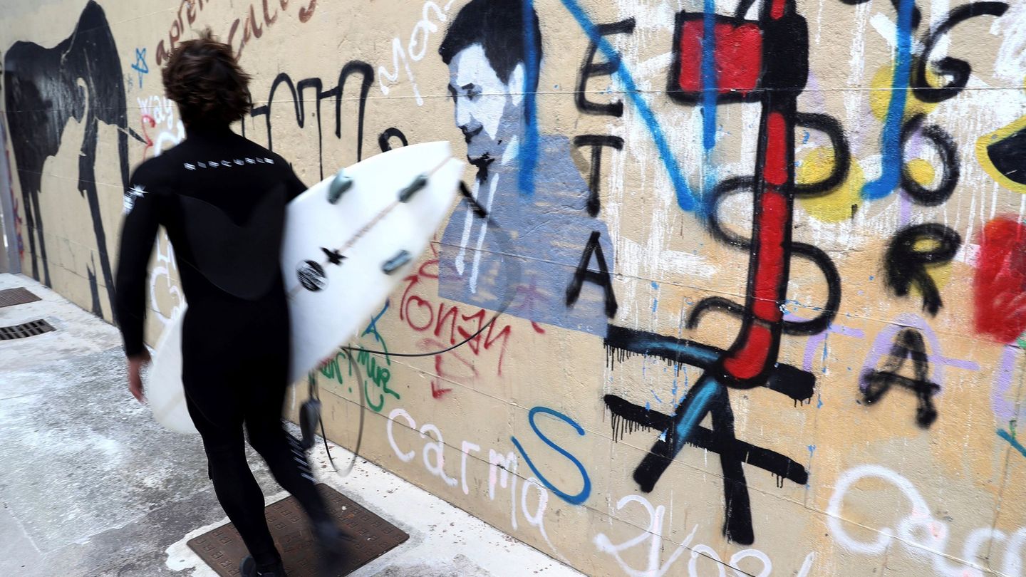 Un surfista pasa junto a una pintada a favor de ETA en el barrio de Gros de San Sebastián. (EFE)
