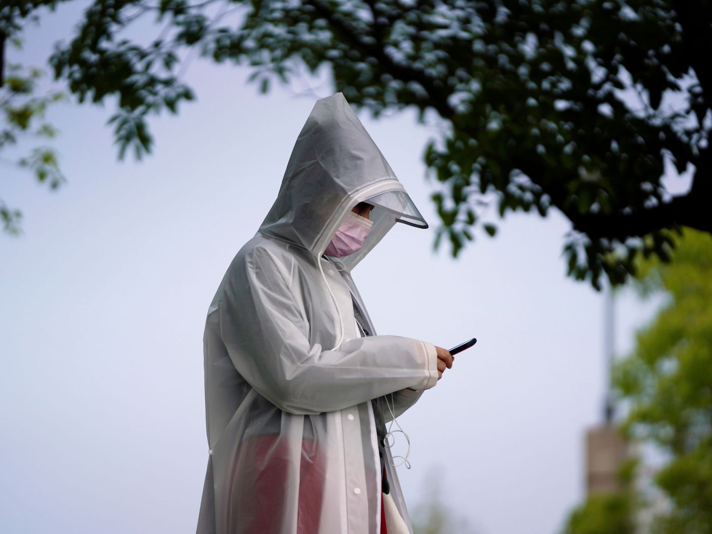 Un residente que usa un equipo de protección revisa su teléfono móvil en Wuhan. (EFE)