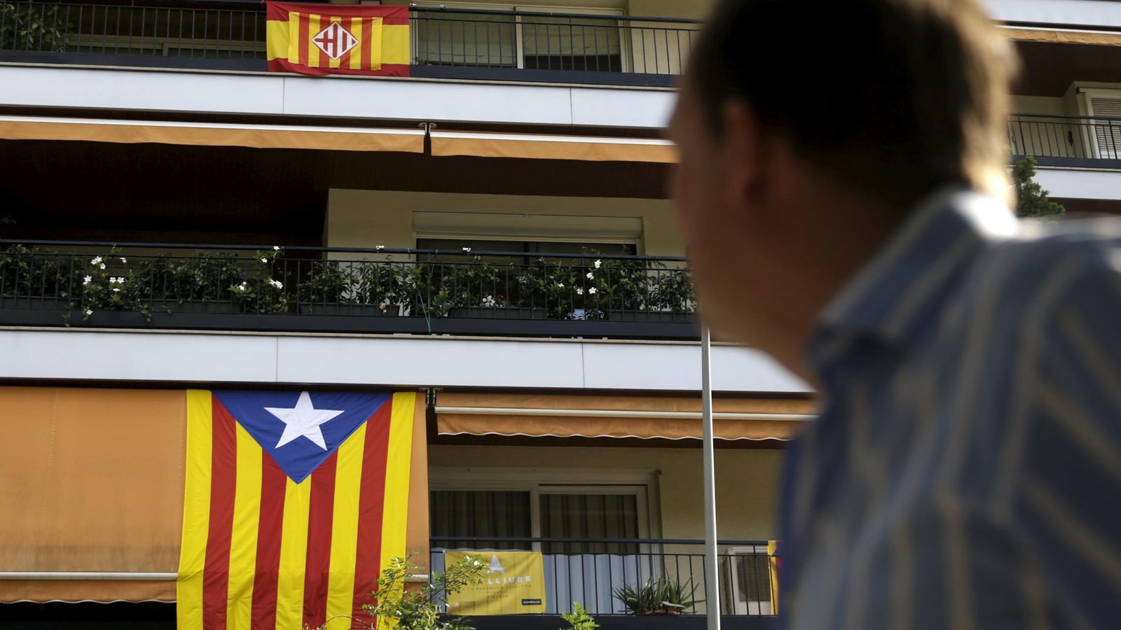 Foto: Un hombre mira la bandera española y una estelada colgadas de una fachada. (Reuters)
