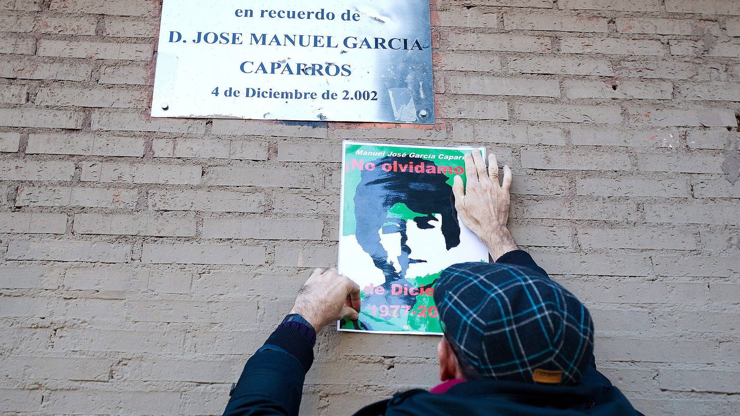 Un hombre pega un cartel con la imagen de García Caparrós debajo de la placa conmemorativa. (EFE)