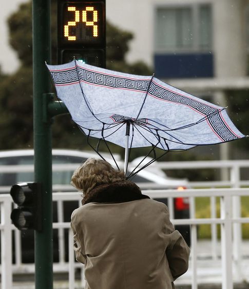 Foto: Una mujer sujeta con sus manos el paraguas para evitar que el viento se lo lleve. (EFE)