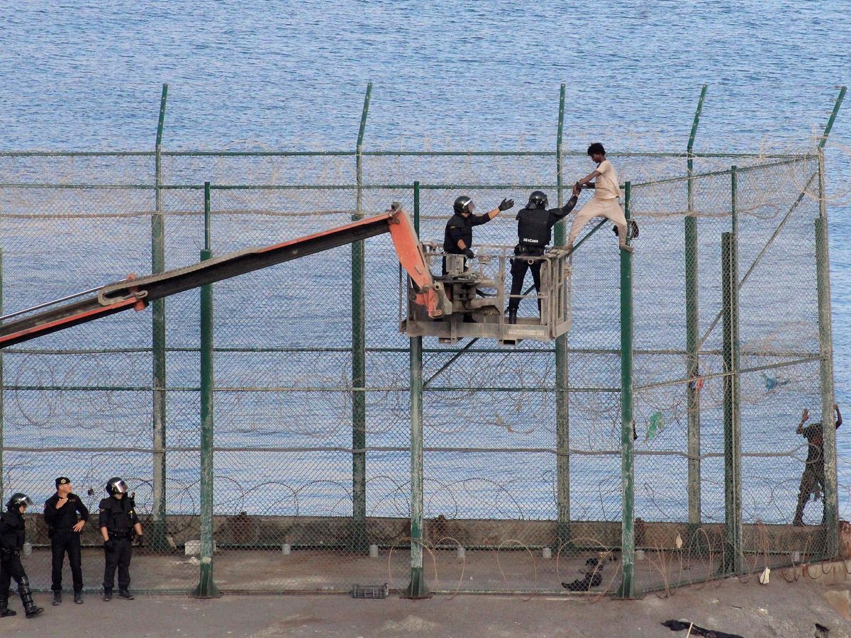 Foto: Un inmigrante subsahariano es detenido por la Policía en la valla fronteriza de Ceuta. (EFE)