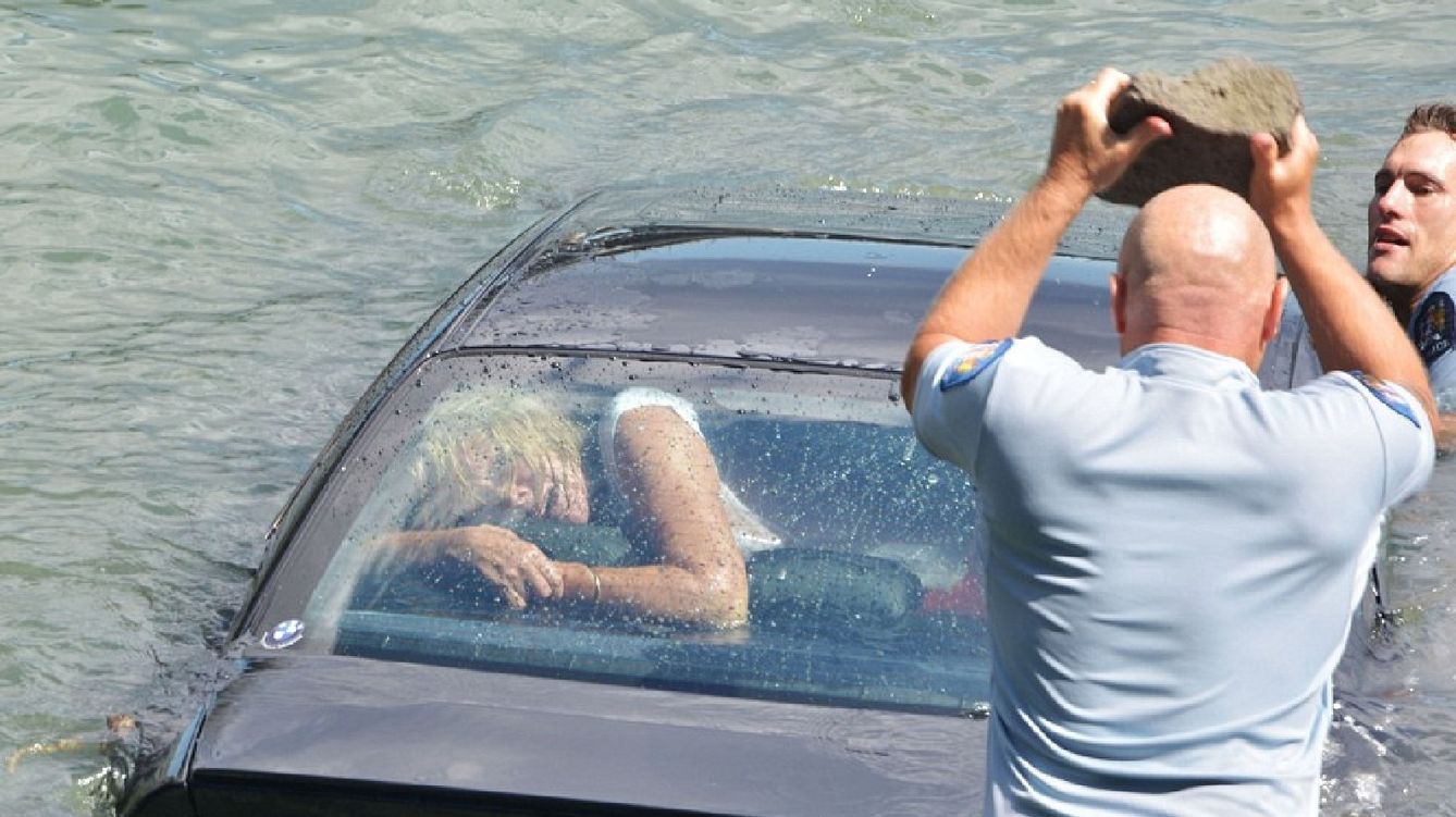 Foto: La mujer rescatada en Nueva Zelanda observa cómo un policía va a romper con una piedra su coche (YouTube)