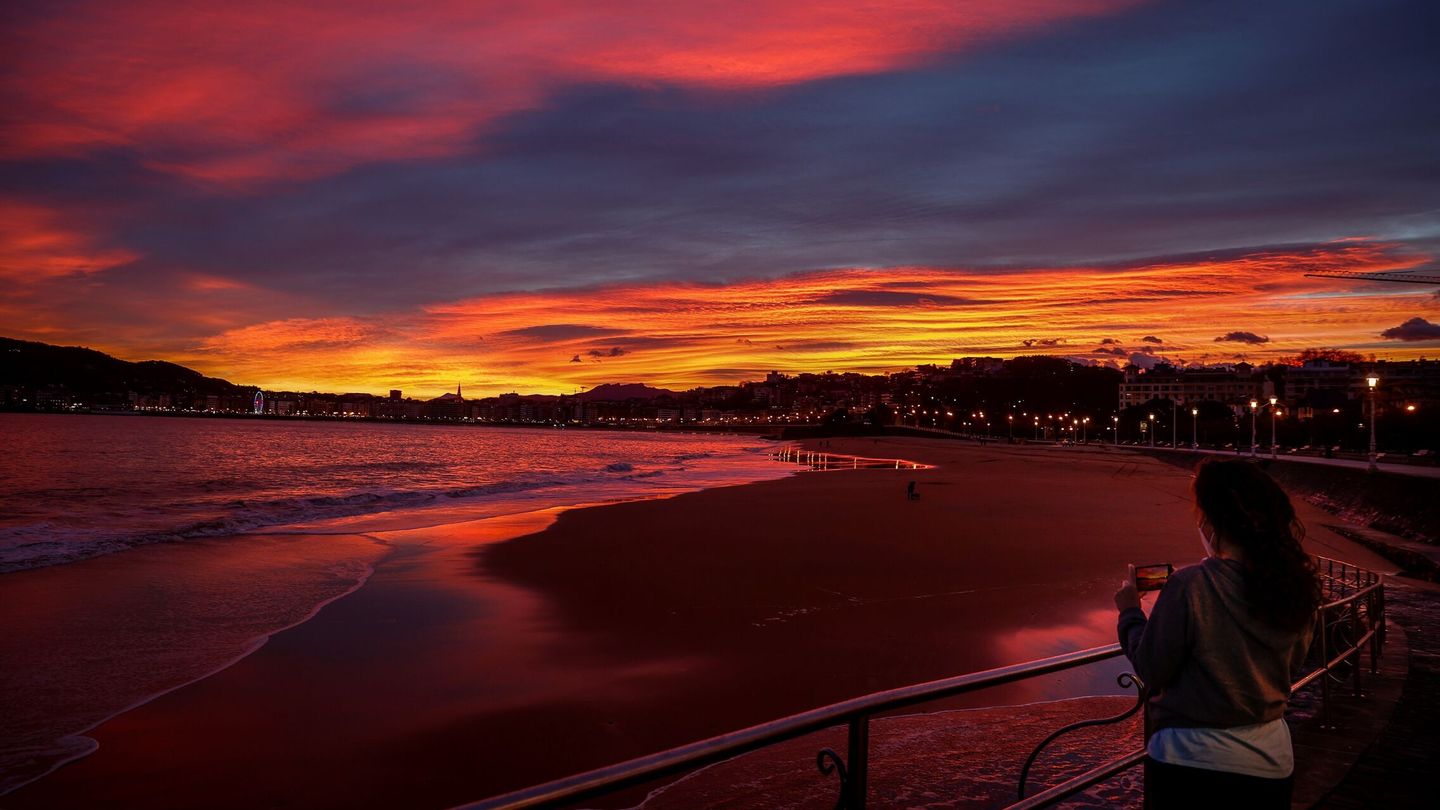 Una joven fotografía el amanecer junto a la playa de Ondarreta de San Sebastián. (EFE/Javier Etxezarreta)