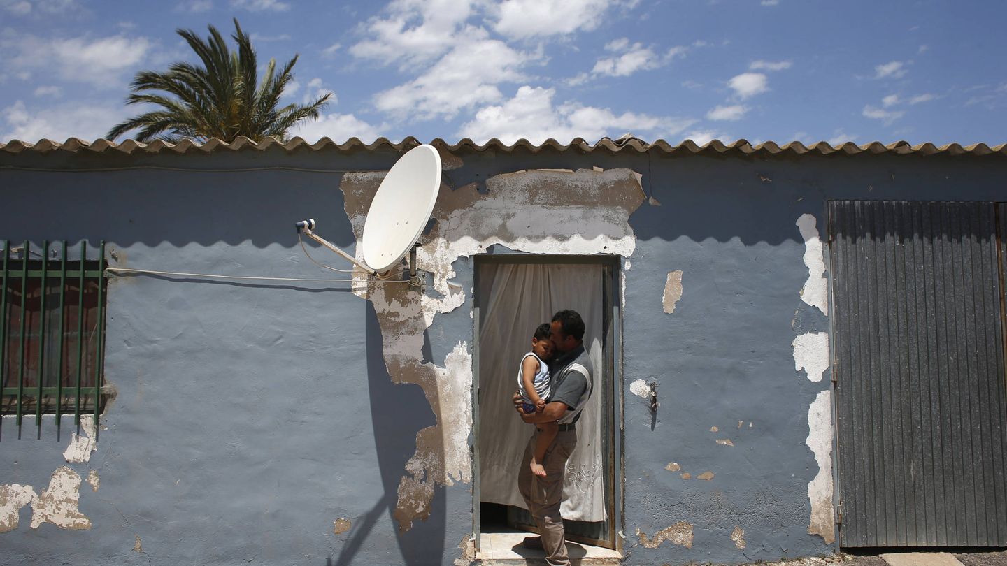 Un jornalero marroquí sostiene a su hijo en una vivienda dentro de una explotación en el campo de Cartagena. (Reuters)
