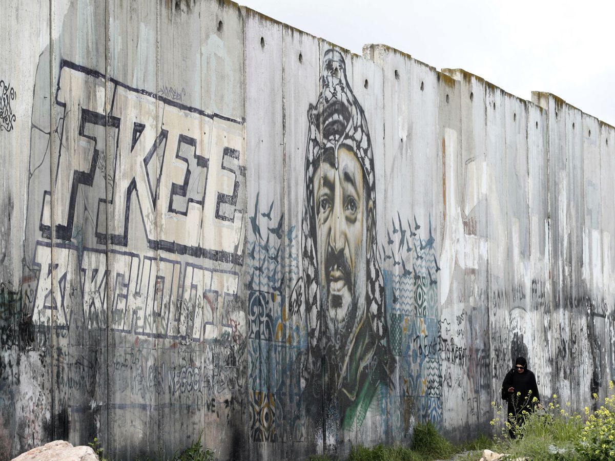 Foto: Una mujer palestina camina cerca de un mural que representa al líder palestino y fundador de Fatah, Yaser Arafat, pintado en una sección de la barrera de separación entre Cisjordania e Israel. (EFE / Alaa Baderneh)