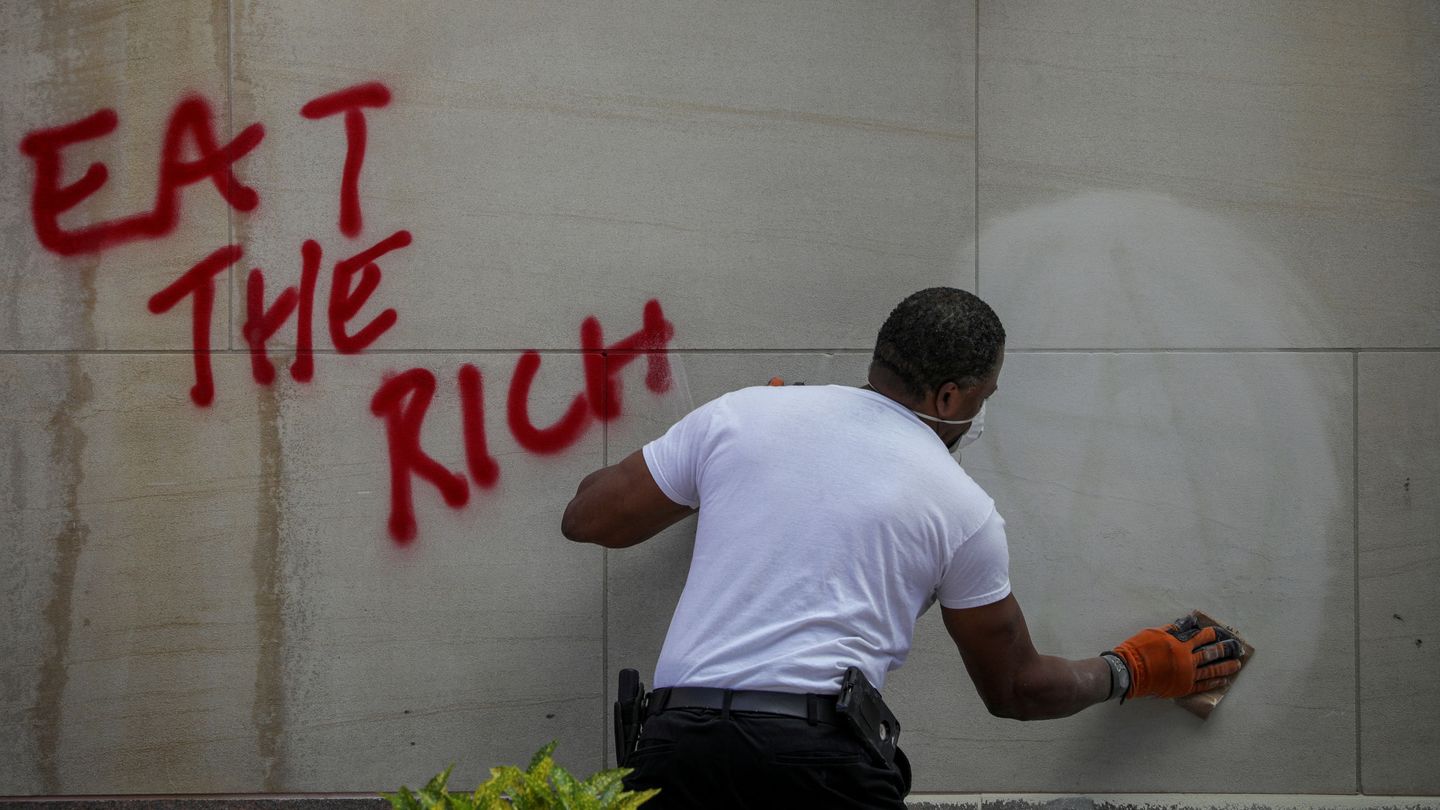 Una persona limpia un grafiti donde pone 'Comerse a los ricos'. (Reuters)