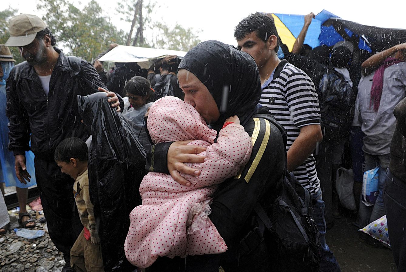 Una refugiada siria sostiene a su bebé bajo la lluvia en la frontera entre Grecia y Macedonia (Reuters). 