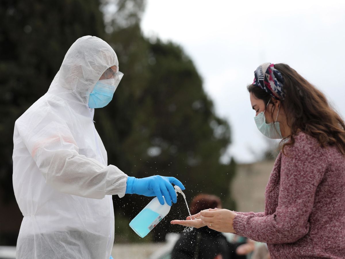 Foto: Un trabajador sanitario dispensa gel desinfectante a una mujer en Jerusalén, Israel (EFE)