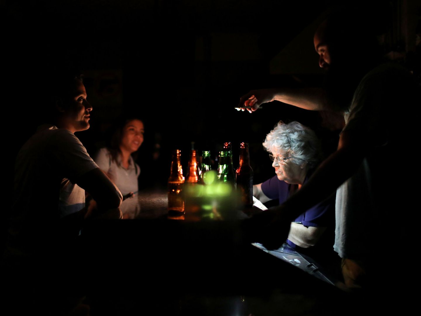 Un hombre utiliza un móvil para alumbrar la mesa de un bar en Caracas. (Reuters)