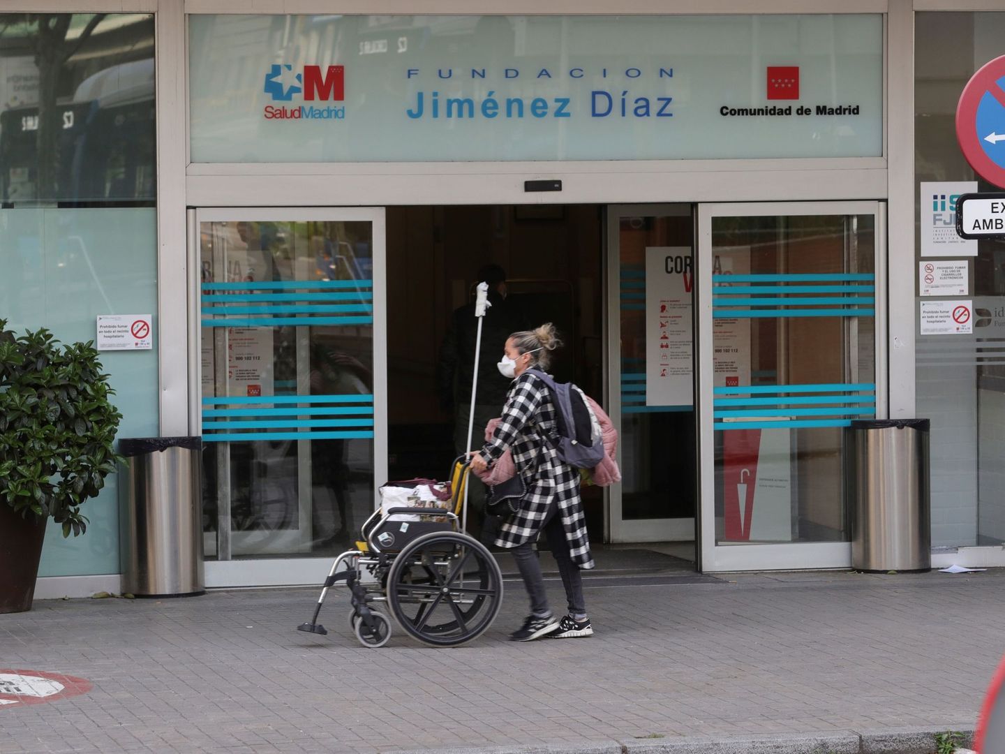 Una mujer con una máscara sanitaria porta una silla de ruedas en los exteriores del Hospital Universitario Fundación Jiménez Díaz de Madrid. (Efe)