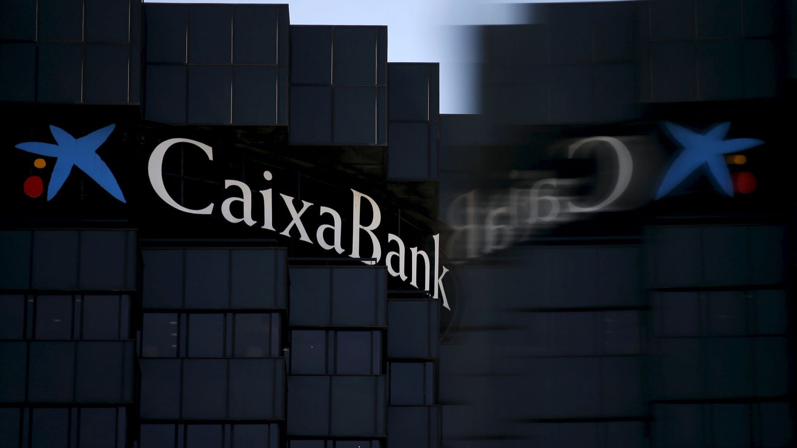 Foto: Caixabank's logo is reflected on a glass of an advertising window, at company's headquarters in barcelona