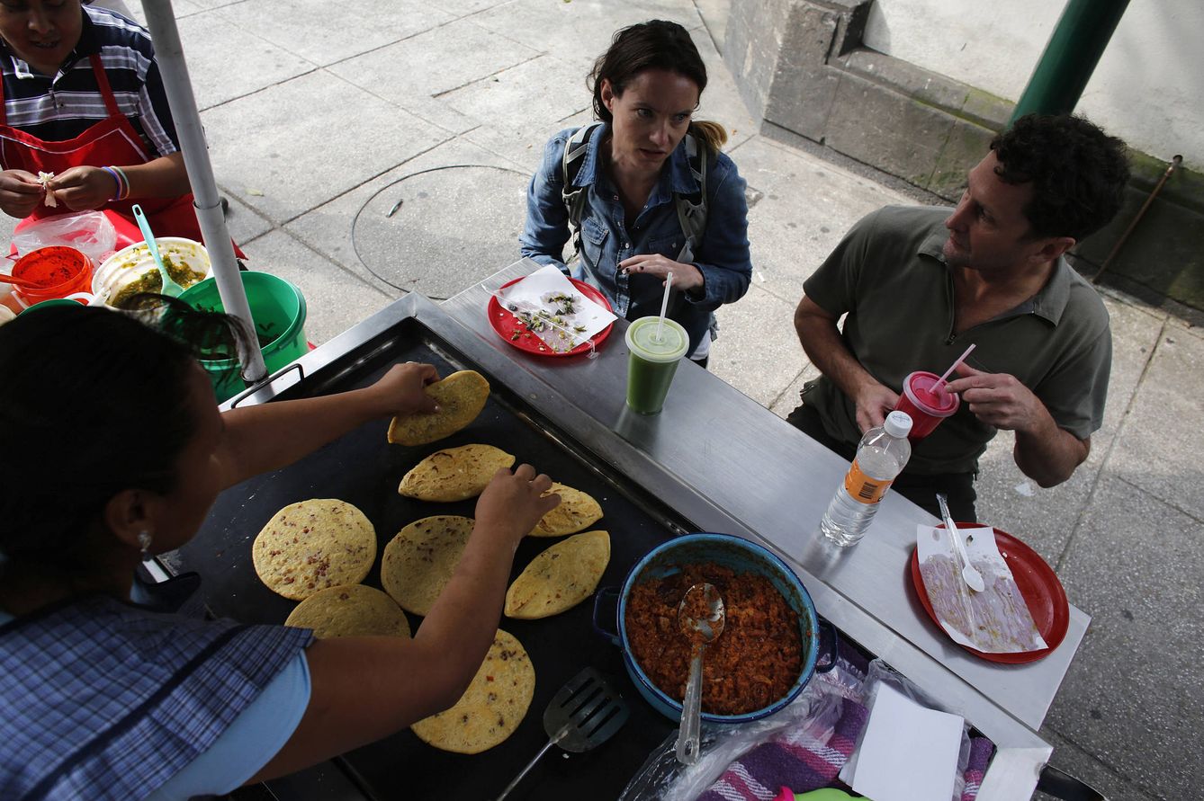 Dos turistas comen tlacoyos en un puesto en Ciudad de México, en octubre de 2013. Muchos platos tradicionales mexicanos, como los nachos con queso, usan 'manchego'. (Reuters)